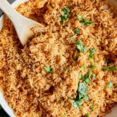 Restaurant style Mexican Rice in a skillet being served with wooden spoon.