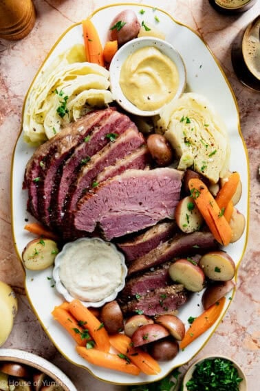 Serving plate with slices of corned beef, cabbage, potatoes, and carrots with dipping sauces.