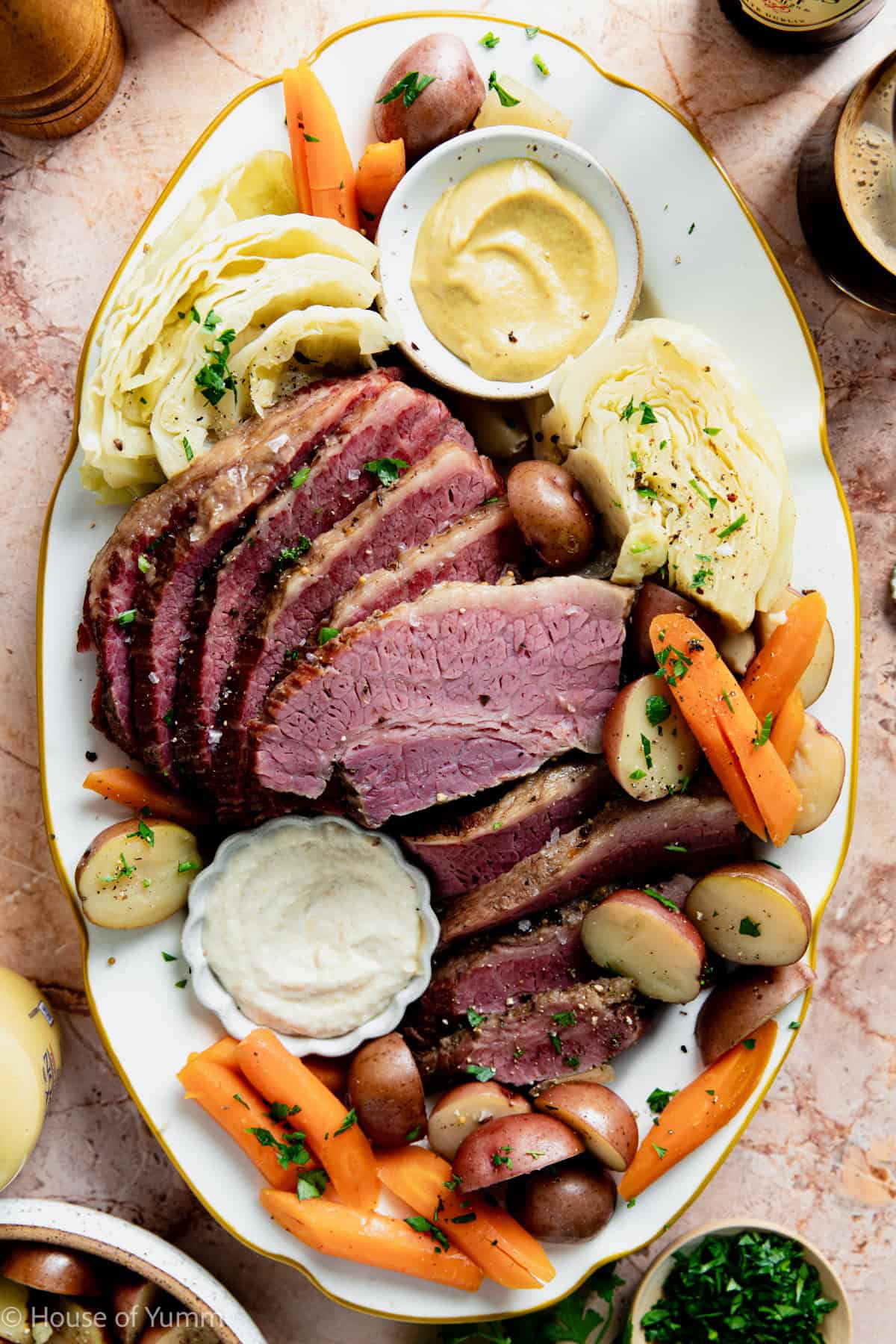 Serving plate with slices of corned beef, cabbage, potatoes, and carrots with dipping sauces.