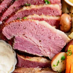 Sliced corned beef on a plate with mustard and horseradish sauce for dipping.