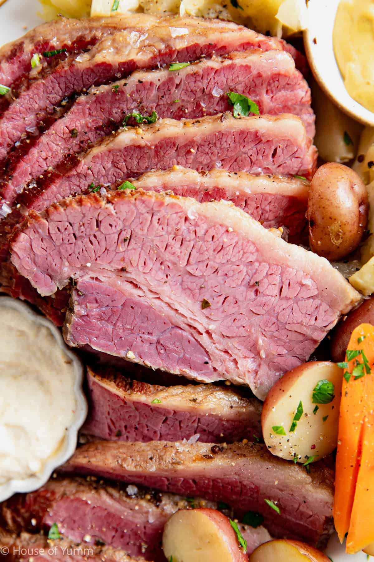 Sliced corned beef on a plate with mustard and horseradish sauce for dipping.