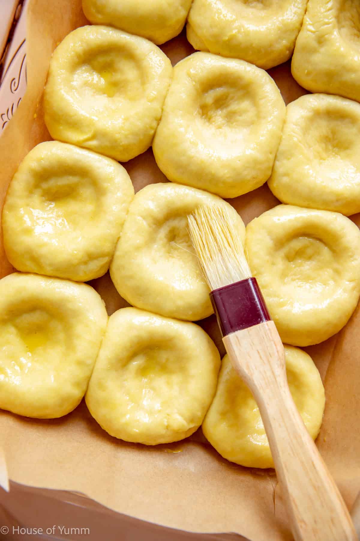 Brushing egg wash on kolache rolls before adding fruit filling.